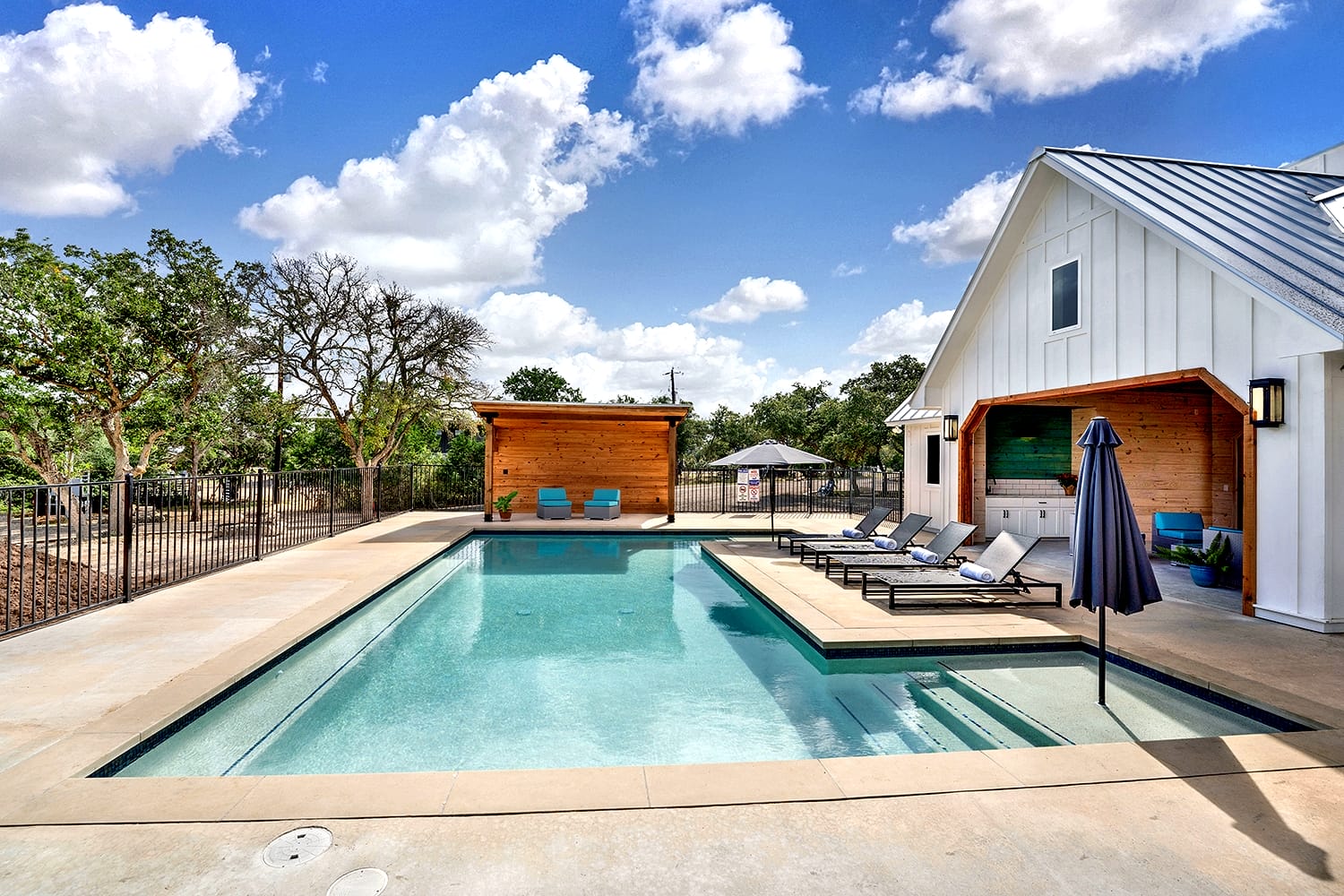 Pool with white farmhouse clubhouse and outdoor seating at Wayside Wimberley